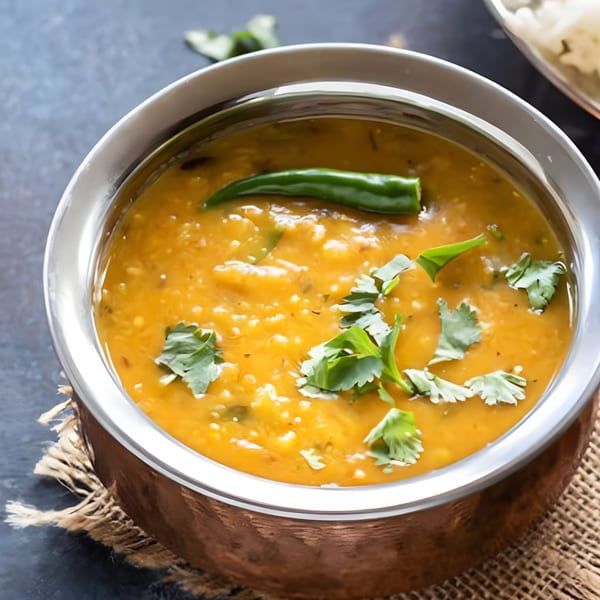 A copper bowl of yellow Indian dal, garnished with green chili and fresh cilantro.