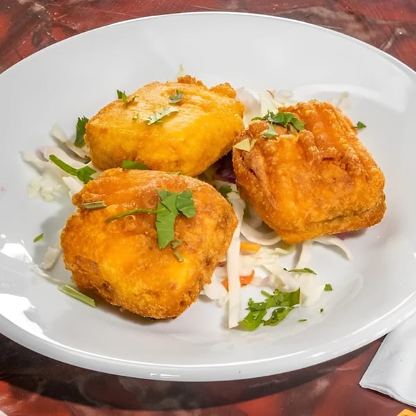 Three golden-fried paneer pakora pieces, garnished with cilantro and served on a bed of shredded cabbage.
