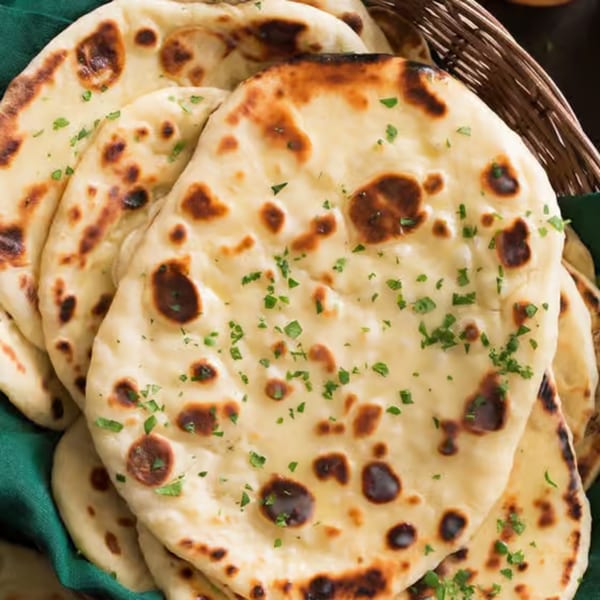A basket of freshly baked Indian naan bread, garnished with parsley, on a green cloth.