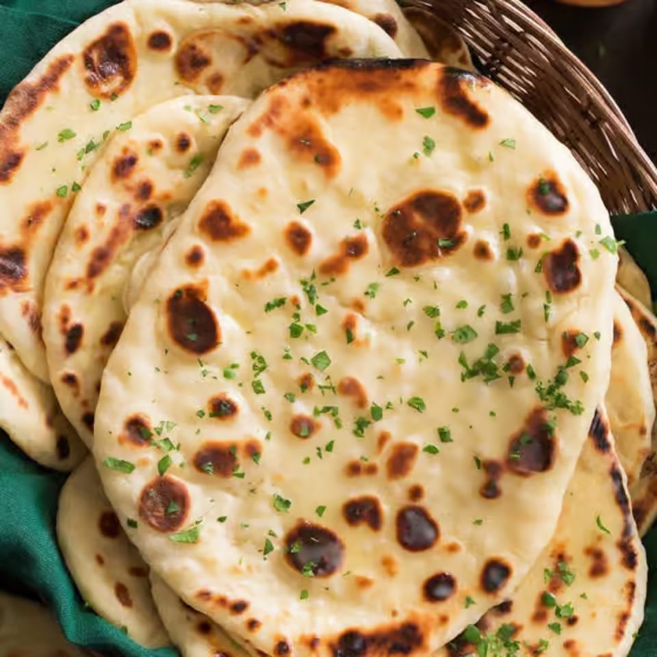 A basket of freshly baked Indian naan bread, garnished with parsley, on a green cloth.