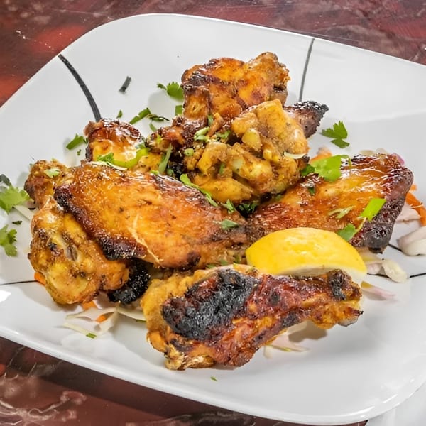 A plate of Mantra Indian Bistro's chicken wings, garnished with cilantro and a lemon wedge.