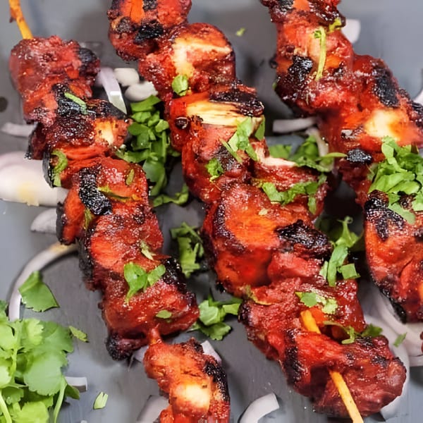 Close-up of vibrant red chicken tikka skewers, garnished with fresh cilantro and sliced onions.