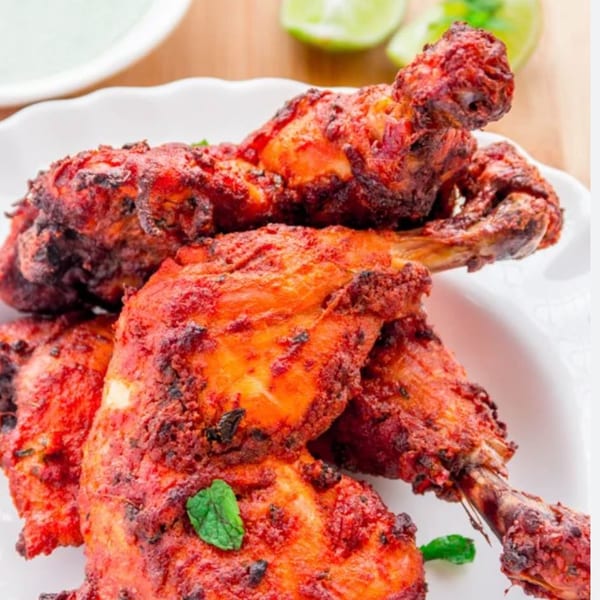 Mantra Indian Bistro's Tandoori Chicken, garnished with mint, on a white plate with lime wedges.