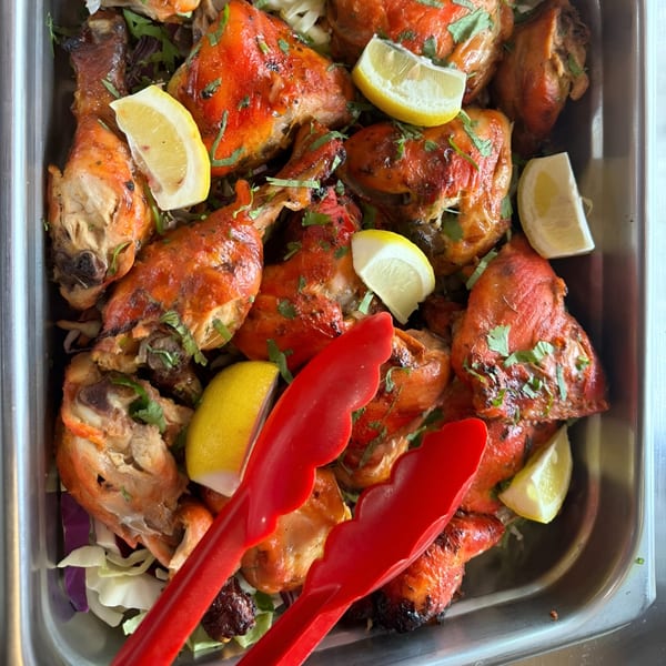 A metal tray filled with vibrant red tandoori chicken pieces, garnished with fresh cilantro and lemon wedges.
