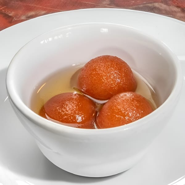 Three gulab jamun, Indian fried dough balls soaked in syrup, in a white bowl.